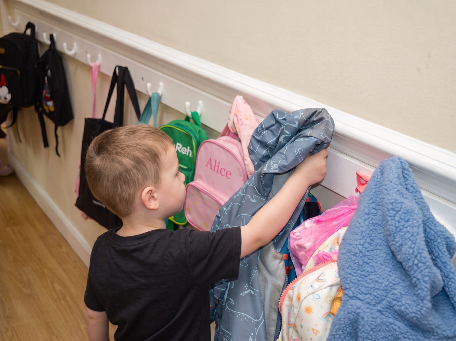 Child hanging up his coat on the nursery pegs