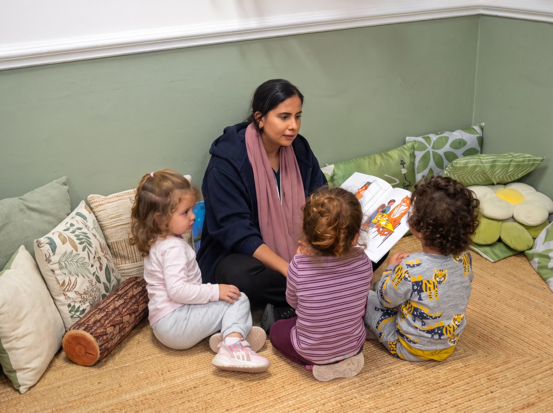 Practitioner reading a picture book with three children in the cosy corner