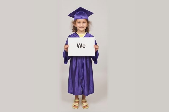 Graduate in cap and gown holding a word card: We