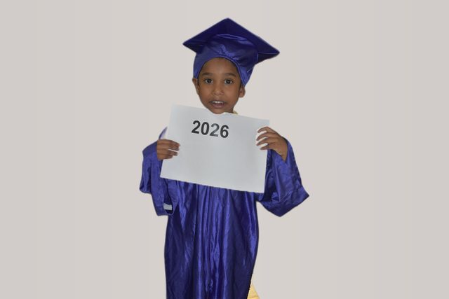Graduate in cap and gown holding a word card: 2026